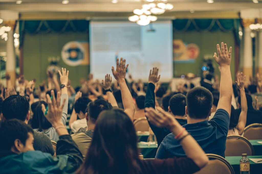 Rear view of Audience showing hand to answer the question from Speaker on the stage